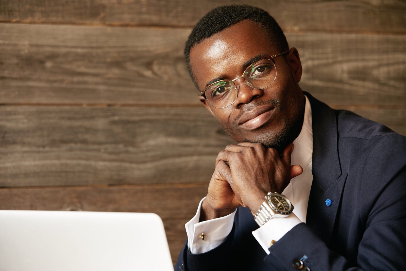 image of african american student of law working on laptop computer, using high internet connection while sitting at the cafe against wooden wall background. handsome smiling young black man